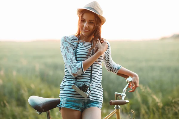 Bella giovane donna si trova in un campo con la sua bicicletta — Foto Stock