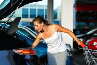 Young woman shifts the purchase from shopping cart in the trunk 