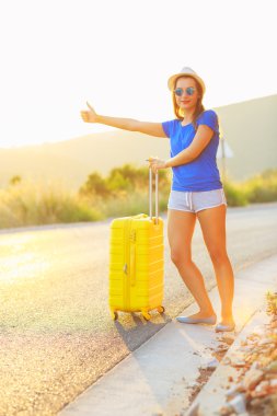 Young woman with a thumb up and yellow suitcase is traveling on 
