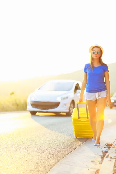 Mladá žena s žlutým kufrem je cestování na silnici hitc — Stock fotografie