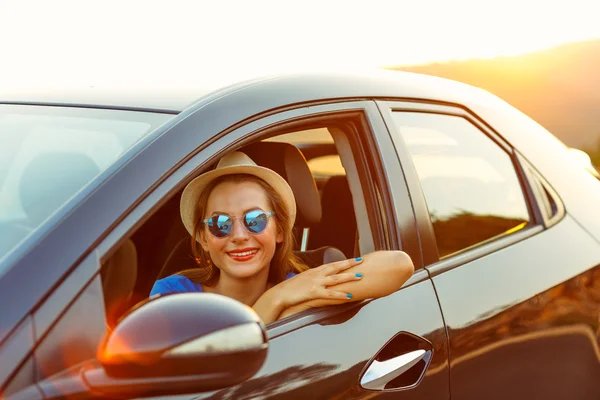 Sorrindo mulher dirigindo um carro ao pôr do sol — Fotografia de Stock