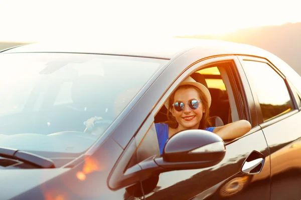 Lächelnde Frau am Steuer eines Autos bei Sonnenuntergang — Stockfoto