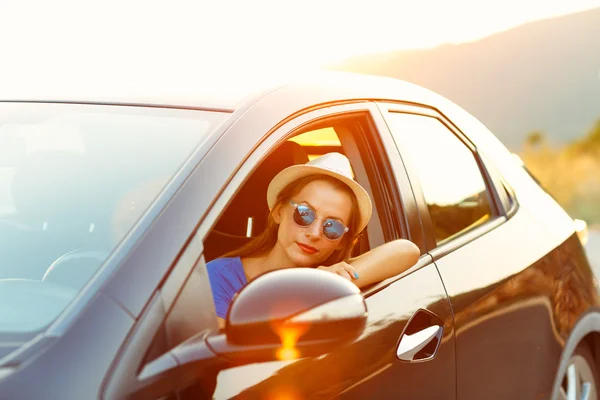Sorrindo mulher dirigindo um carro ao pôr do sol — Fotografia de Stock