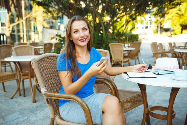 Young pretty modern blogger using smartphone and makes notes in — Stock Photo, Image