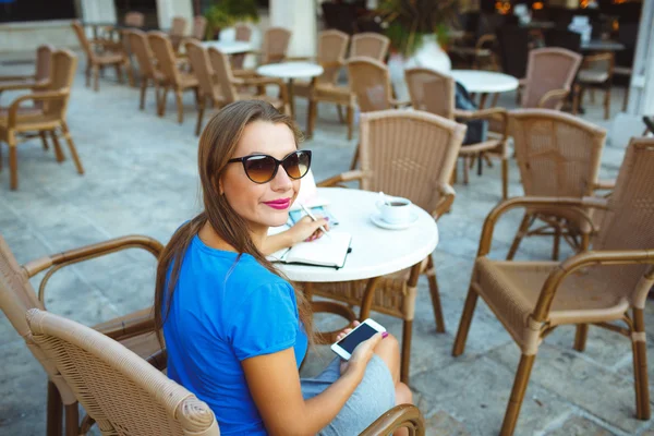 Young pretty modern blogger using smartphone and makes notes in — Stock Photo, Image