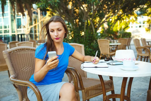Young pretty modern blogger using smartphone and makes notes in — Φωτογραφία Αρχείου