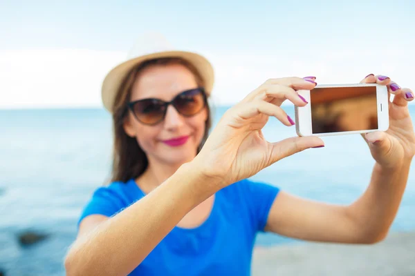 Chica en el sombrero haciendo selfie por el teléfono inteligente en el backgroun — Foto de Stock