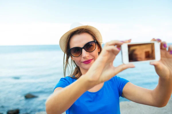 Chica en el sombrero haciendo selfie por el teléfono inteligente en el backgroun — Foto de Stock