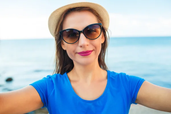 Chica en el sombrero haciendo selfie por el teléfono inteligente en el backgroun — Foto de Stock