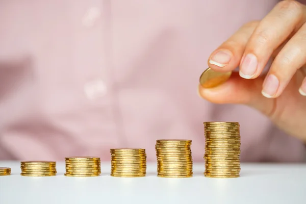 Mano femenina apilando monedas de oro en columnas crecientes — Foto de Stock