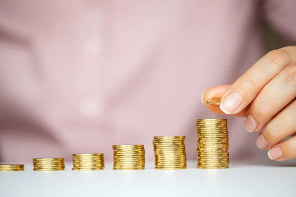 Female hand stacking gold coins into increasing columns — Stock Photo, Image