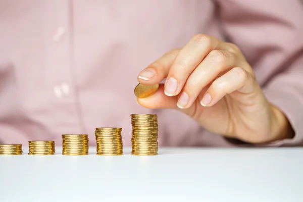 Female hand stacking gold coins into increasing columns — Stock Photo, Image