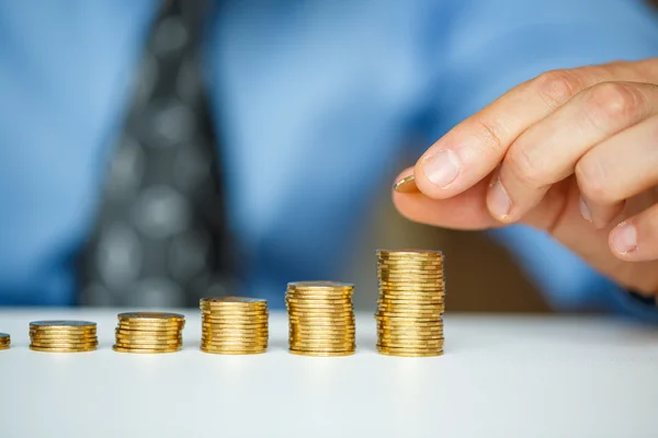 Mano masculina apilando monedas de oro en columnas crecientes — Foto de Stock