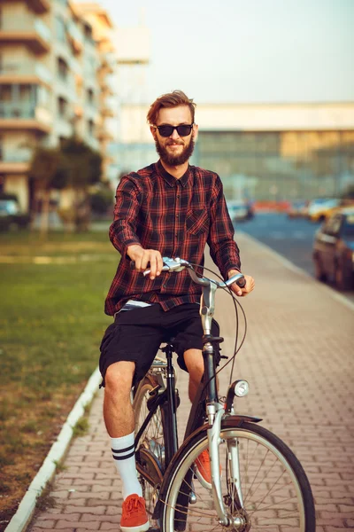 Stylish man in sunglasses riding a bike on city street — Stock Photo, Image