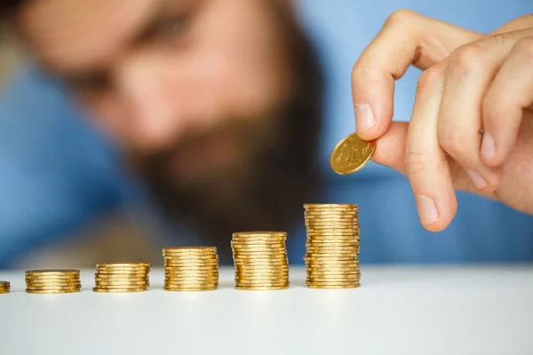 Hombre barbudo apilando monedas de oro en columnas crecientes — Foto de Stock