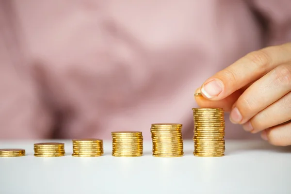 Mano femenina apilando monedas de oro en columnas crecientes — Foto de Stock