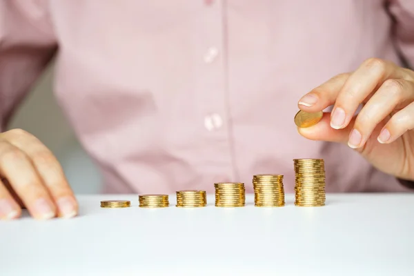 Mano femenina apilando monedas de oro en columnas crecientes — Foto de Stock