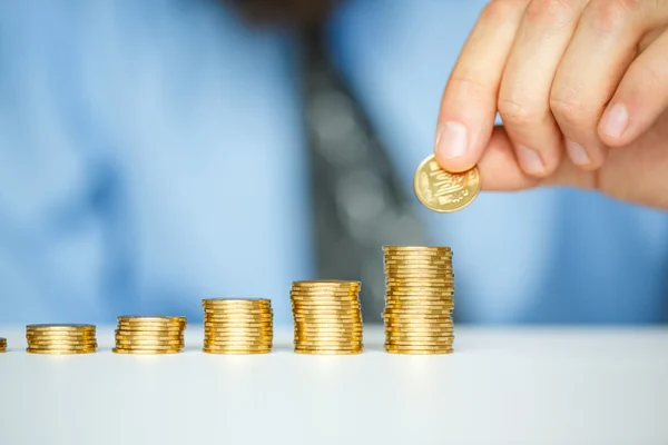 Male hand stacking gold coins into increasing columns — Stock Photo, Image