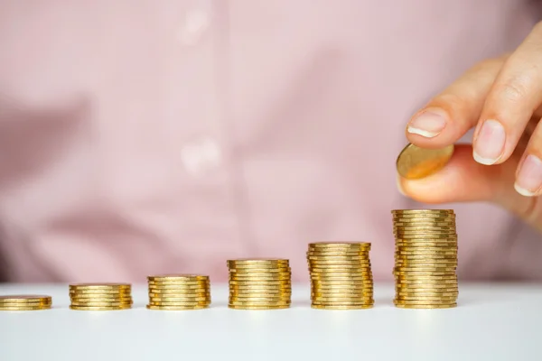 Mano femenina apilando monedas de oro en columnas crecientes — Foto de Stock