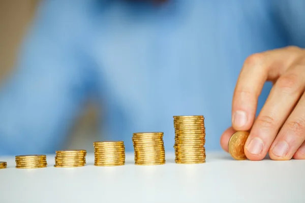 Mano masculina apilando monedas de oro en columnas crecientes — Foto de Stock