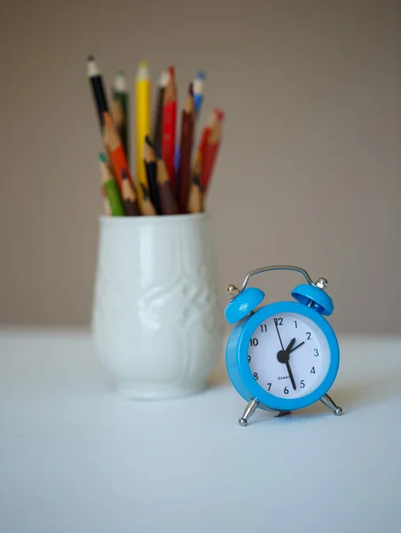 Pequeño reloj despertador azul y un vaso con lápices de colores en una ta — Foto de Stock