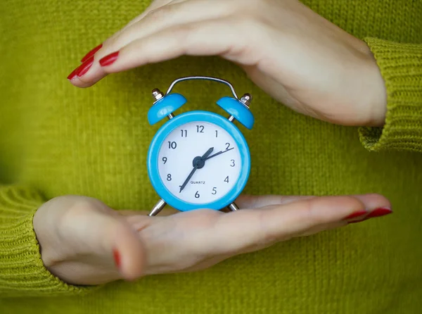 Pequeño despertador azul en las manos de las mujeres —  Fotos de Stock