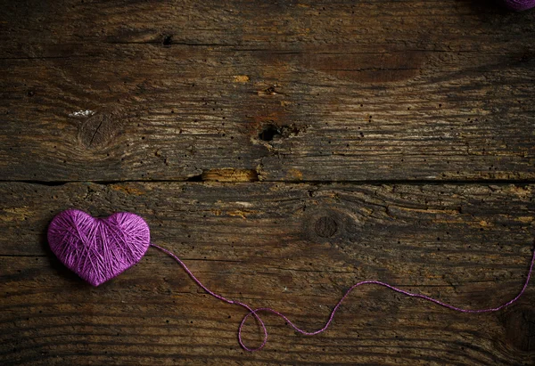 Purple Heart with a ball of thread on on old shabby wooden backg