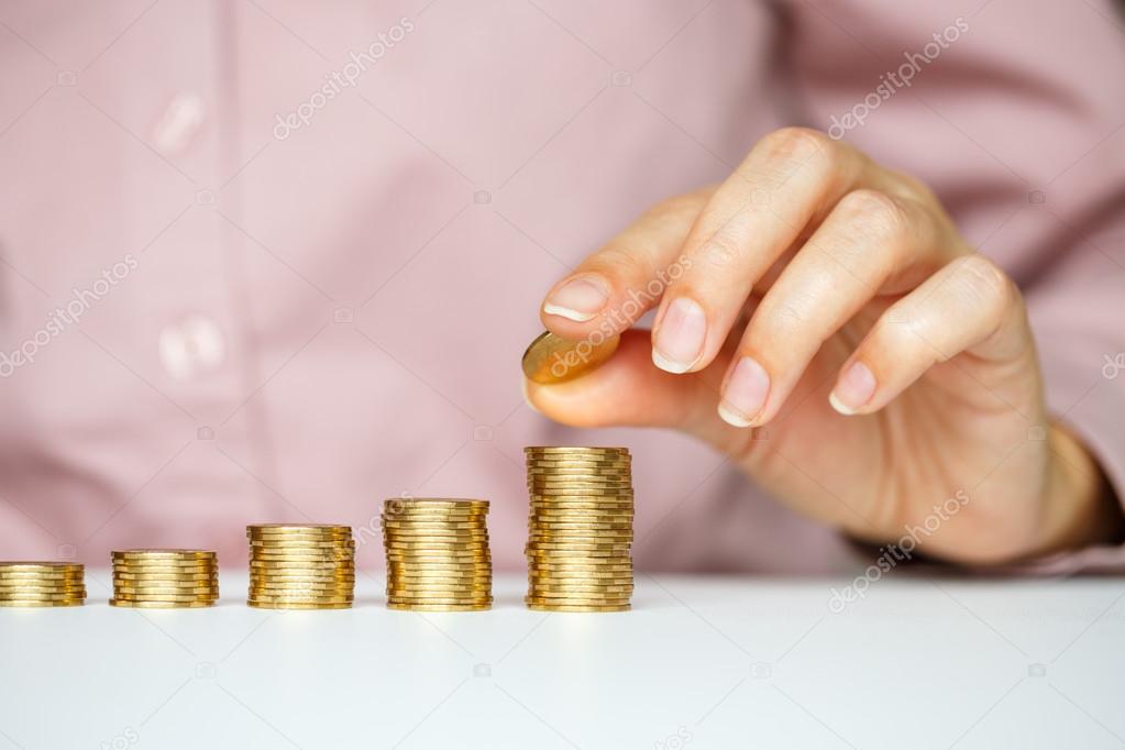 Female hand stacking gold coins into increasing columns