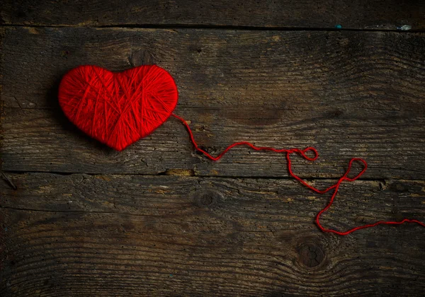 Forma de coração vermelho feito de lã no velho fundo de madeira gasto — Fotografia de Stock