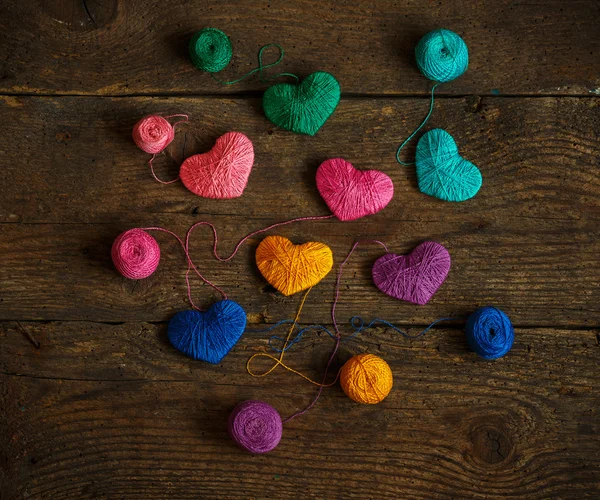 Corazones multicolores con bolas de hilo en madera vieja y rastrera — Foto de Stock