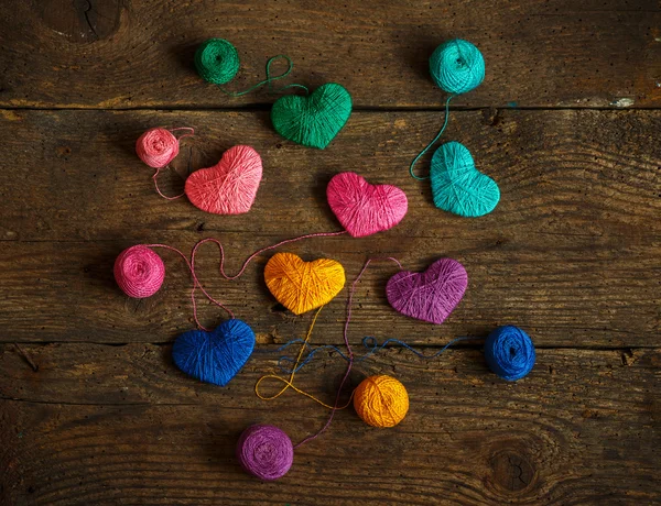 Corazones multicolores con bolas de hilo en madera vieja y rastrera — Foto de Stock