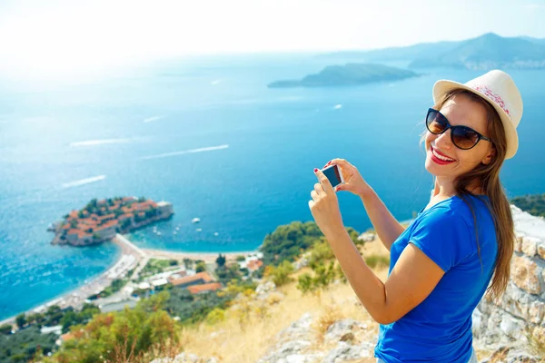 Chica en el sombrero haciendo fotos por el teléfono inteligente cerca de la isla —  Fotos de Stock