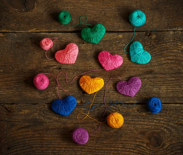 Corazones multicolores con bolas de hilo en madera vieja y rastrera — Foto de Stock