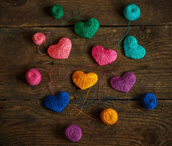 Corazones multicolores con bolas de hilo en madera vieja y rastrera — Foto de Stock