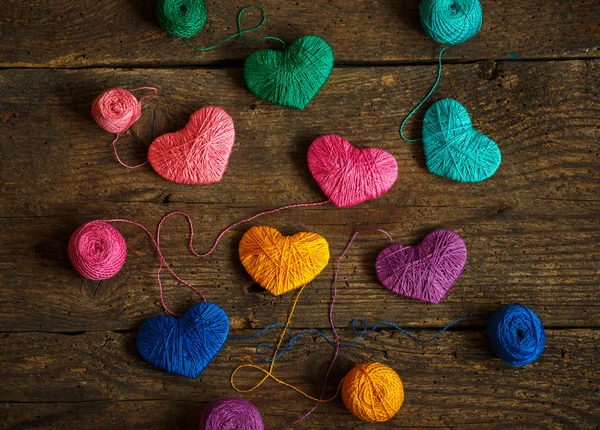 Corazones multicolores con bolas de hilo en madera vieja y rastrera — Foto de Stock