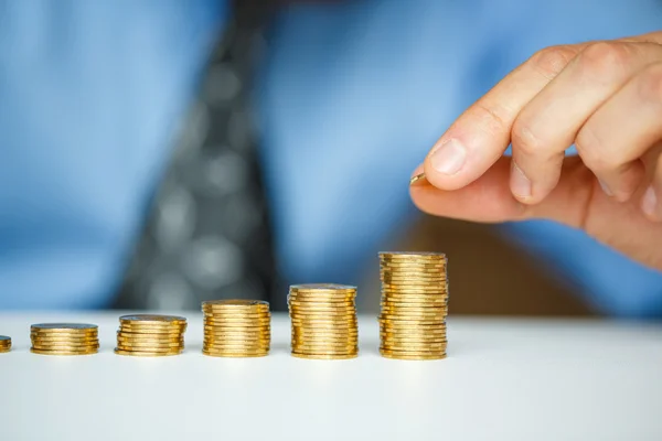 Male hand stacking gold coins into increasing columns — Stock Photo, Image