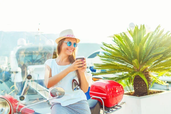 Trendy kadın üzerinde onun kırmızı motosiklet yakınındaki paket servisi olan restoran kahve içme — Stok fotoğraf