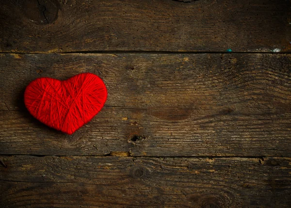 Forma de coração vermelho feito de lã no velho fundo de madeira gasto — Fotografia de Stock