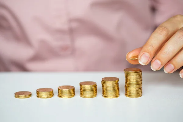 Mano femenina apilando monedas de oro en columnas crecientes — Foto de Stock