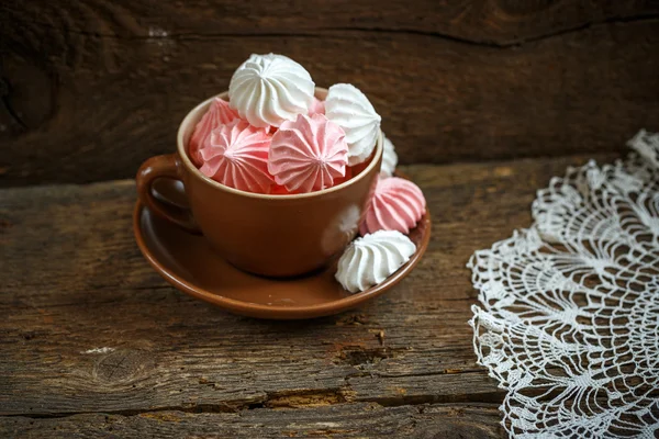 Розовые и белые безе в чашке на старом деревянном фоне — стоковое фото