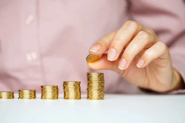 Mão feminina empilhando moedas de ouro em colunas crescentes — Fotografia de Stock