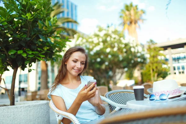 Jeune jolie femme se détendre dans le café en plein air et en utilisant smartp — Photo