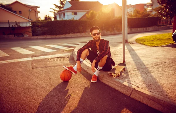 Pemuda bergaya dengan bola basket dan skateboard duduk di — Stok Foto