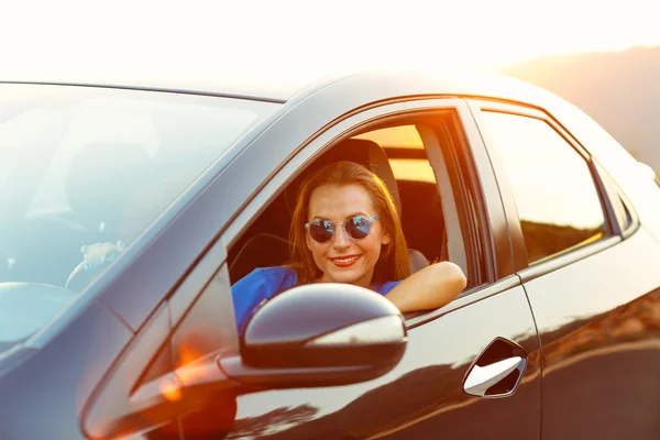 Lächelnde Frau am Steuer eines Autos bei Sonnenuntergang — Stockfoto