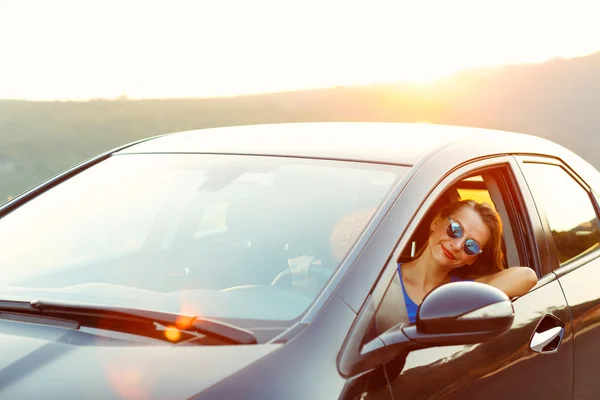 Donna sorridente alla guida di una macchina al tramonto — Foto Stock