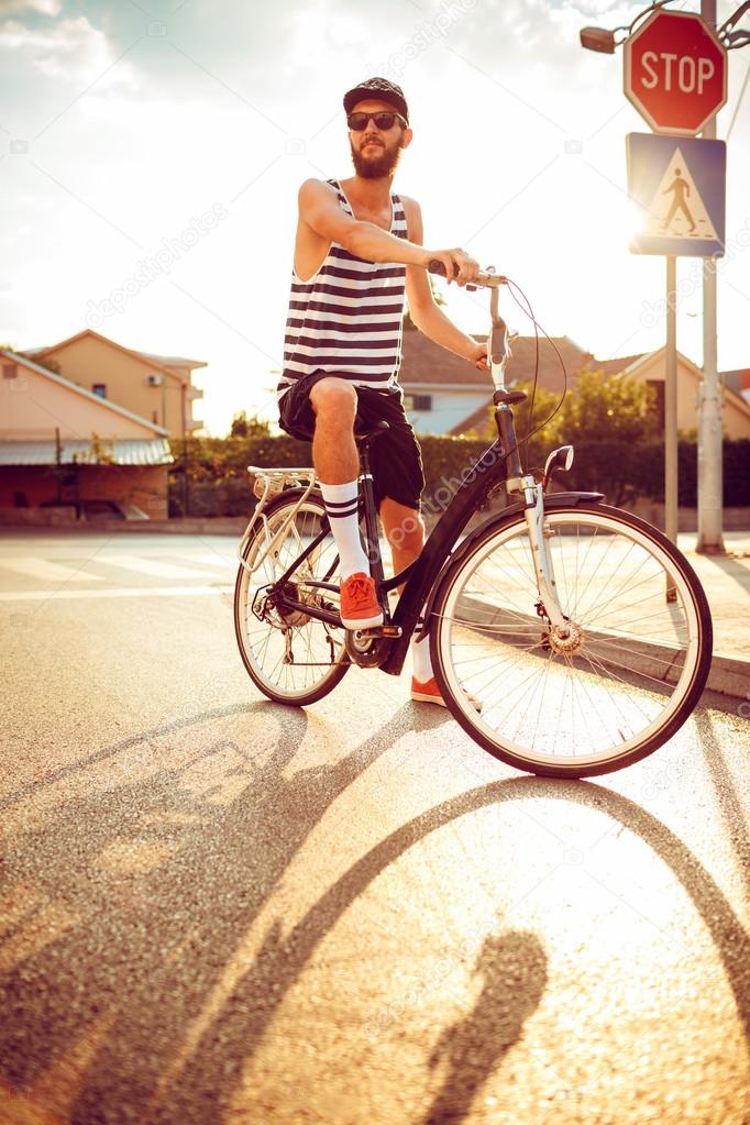 Young man in sunglasses riding a bicycle on a city street at sun