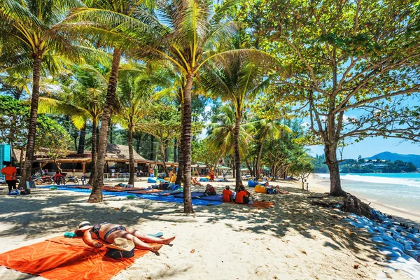 Tourists sunbathing on the sand of a tropical beach in the shade — Stock Photo, Image