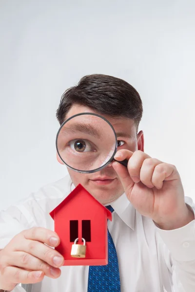 Man with a magnifying glass and paper house Stock Picture