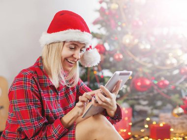 Yılbaşı ağacının önünde tablet kullanan kadın.