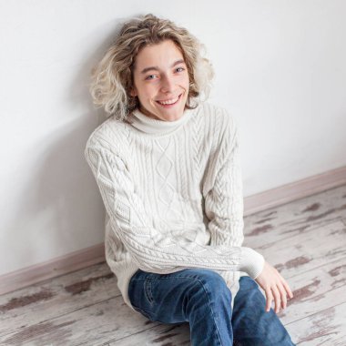 Sarışın çocuk duvarın yanında oturuyor. Genç, mutlu, genç